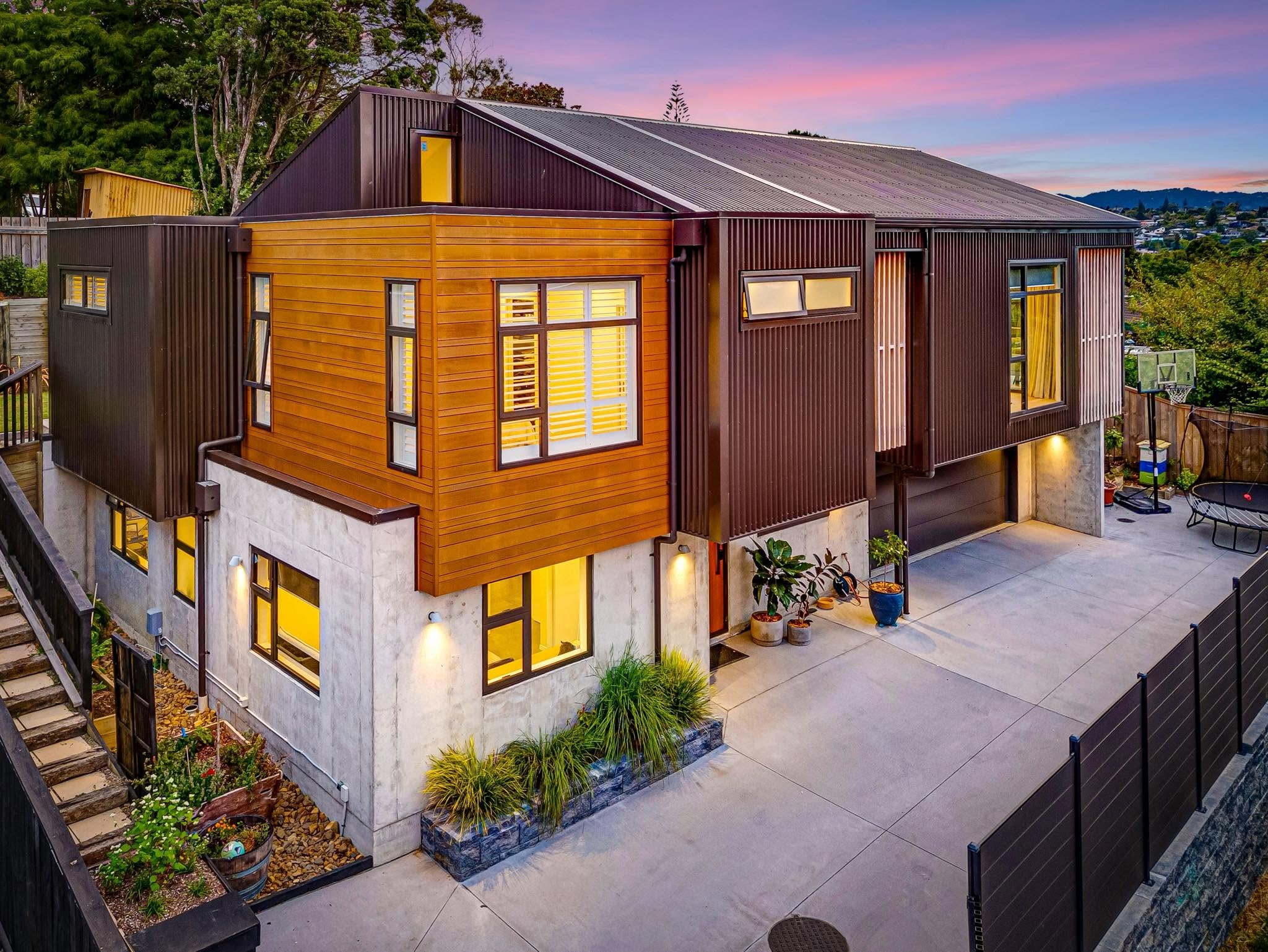 Modern Auckland home built with timber, concrete, and dark metal cladding at dusk